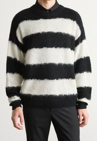 Czarnobiały sweter w paski o puszystej fakturze. Posiada okrągły dekolt, luźny krój oraz długie rękawy. Paski mają różną szerokość.