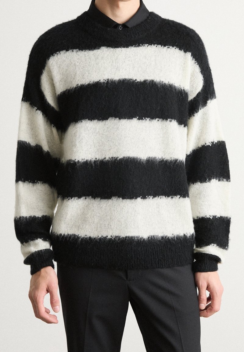 Czarnobiały sweter w paski o puszystej fakturze. Posiada okrągły dekolt, luźny krój oraz długie rękawy. Paski mają różną szerokość.