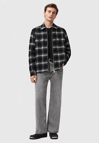 Fekete és szürke kockás flanel ing gombos záródással, szürke bőszárú farmernadrággal és fekete cipővel párosítva. Egyszerű, texturált minták mindenütt.