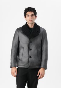 Cappotto in shearling grigio con colletto nero testurizzato, chiusura frontale a bottoni, due tasche laterali e vestibilità morbida. Finitura liscia simile alla suede.