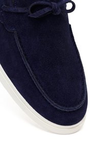 Zbliżenie na granatowy zamszowy but casualowy z białą podeszwą i zawiązanymi sznurowadłami, ukazujący szczegółowe przeszycia na cholewce.