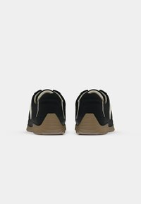 Paire de chaussures décontractées noires et beiges vues de dos avec des semelles marron texturées sur un fond blanc uni.