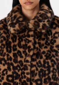 Nepbont jas met luipaardprint, voorzien van een brede kraag, zachte textuur en donkerbruine en zwarte vlekken op een beige achtergrond.