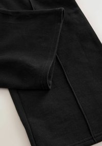 Schwarze Baumwollleggings mit glatter Textur, lang tapered Bein und genähten Nähten. Keine sichtbaren Muster oder Hardware-Akzente.
