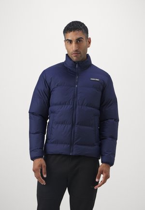 Navy puffer jacket with a high collar, featuring a front zipper and stitched panels, made from a smooth, insulated fabric.