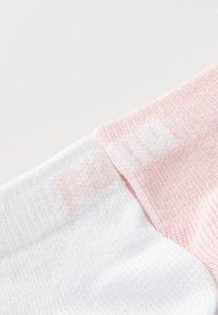 Calcetines deportivos blancos y rosas con textura acanalada, que cuentan con un logo blanco en la sección rosa. Tejido suave, diseñado para la comodidad.