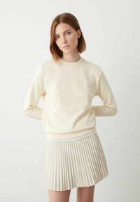 Lichtcrème sweatshirt met ronde hals en lange mouwen, gecombineerd met een plissé beige rok. Gladde textuur, minimalistisch design.