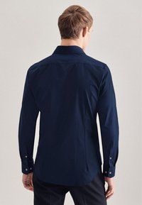 Maglietta blu navy a maniche lunghe, design aderente, orlo curvato, polsini con bottoni, texture liscia, tessuto morbido con dettagli di cucitura minimali.