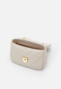 Bolso de mano acolchado en beige con un acento de hardware cuadrado dorado, que cuenta con un cierre de cremallera y un interior suave, diseñado para el estilo y la funcionalidad.