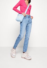 Svetle modré džíny, růžové tričko s dlouhým rukávem a mohutné tenisky s bílými, růžovými a levandulovými detaily. Malá modrá kabelka přes rameno se zipem.