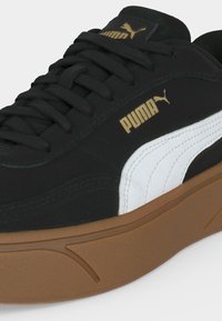Μαύρο αθλητικό παπούτσι Puma με λευκή πλαϊνή ρίγα, καφέ λαστιχένια σόλα, μαύρα κορδόνια και χρυσό λογότυπο Puma στο πλάι και στη γλώσσα.