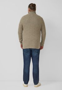 Beige gebreide trui met een hoge kraag, voorzien van een reliëfgeometrisch patroon; gecombineerd met blauwe spijkerbroek en witte sneakers.