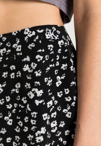 Svart tygkjol med vitt blommönster, med en CK-logotyp på midjan. Slät textur och skräddarsydd passform.