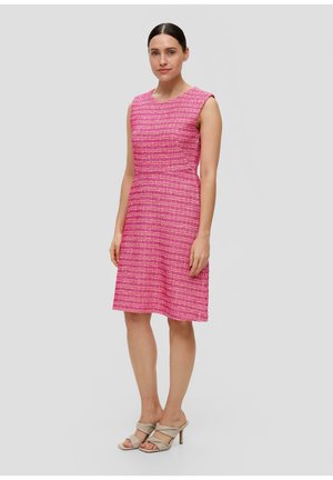 Robe sans manches rose avec un motif texturé et une taille cintrée. La robe arrive au-dessus du genou, accompagnée de chaussures à talons sveltes de couleur claire.
