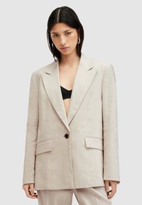 Blazer in lino beige con un design strutturato, ampi revers, chiusura con un solo bottone nero e due tasche frontali. Stile minimalista.