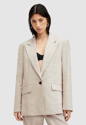 Blazer de lino beige con un diseño estructurado, solapas anchas, cierre de un solo botón negro y dos bolsillos frontales. Estilo minimalista.