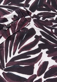 T-shirt à manches courtes en tissu doux et respirant, présentant un motif de feuilles violet foncé et blanc, avec un col rond et deux boutons noirs à l'épaule.