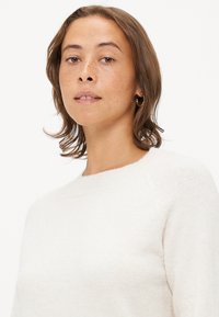 Suéter beige claro con cuello redondo, textura suave y mangas raglán, con costuras mínimas y un ajuste holgado.