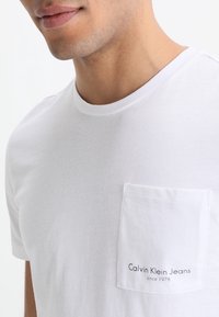 Vit bomull t-shirt med rund halsringning och en ficka på vänster bröst med trycket "Calvin Klein Jeans sedan 1978" i svart.