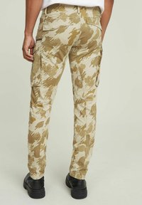 Spodnie cargo w beżowym wzorze kamuflażu, wykonane z trwałej tkaniny, z bocznymi kieszeniami, dopasowanymi nogawkami i luźnym krojem.