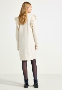 Creme strikdress med flæse detaljer på skuldrene, lange ærmer og en mellemlang længde. Matchet med sorte ankelstøvler og strømpebukser.