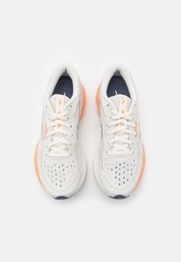 Chaussures de course blanches avec des accents orange, tige en maille texturée, bout arrondi et intérieur bleu marine, dotées de perforations pour la respirabilité.