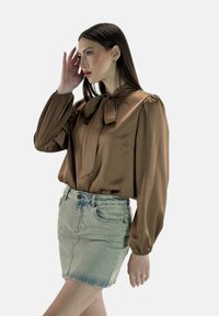 Brun satinbluse med pufærmer og en sløjfedetalje, kombineret med en lyseblå denimmininederdel. Glat tekstur, løs pasform.