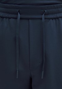 Granatowe spodnie dresowe z elastycznym pasem, z teksturowaną powierzchnią i kontrastowym sznurkiem. Prosty krój, idealny na codzienne okazje.