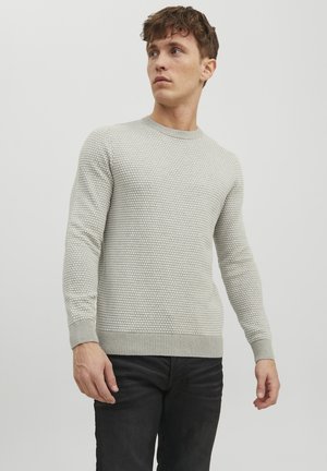 Suéter de punto gris claro con un patrón texturizado, puños y dobladillo acanalados, usado sobre unos jeans negros. Cuello redondo simple.