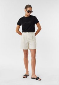 Czarna koszulka z napisem "SAFARI", kremowe szorty z zakładkami i czarne klapki; gładkie tekstury, prosty design, neutralne kolory.