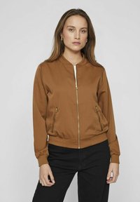 Hnedá bombardérka vyrobená z hladkej látky s predným zipsom, bočnými vreckami, rebrovanými manžetami a spodným lemom, ozdobená zlatými kovovými akcentmi.