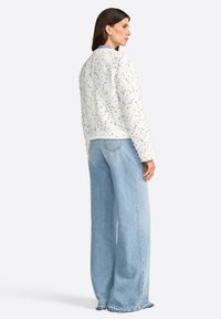 Weißer strukturierter Blazer mit bunten Flecken, rundem Ausschnitt und gerippten Säumen, kombiniert mit hochgeschnittenen hellblauen weit geschnittenen Jeans.