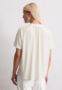 Haut crème à manches courtes avec un col rond et des détails froncés à l'arrière. Tissu lisse avec une coupe décontractée et un ourlet.