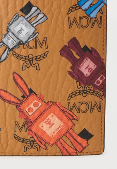 Καφέ φόντο με υφή που παρουσιάζει καρτουνίστικα σχέδια κουνελιών σε κόκκινο, μπλε και ροζ, με λογότυπα "MCM" και παιχνιδιάρικο αισθητικό στυλ patchwork.