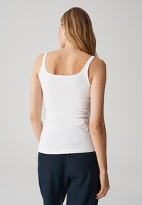 Top bianco senza maniche con scollatura a V sul retro, realizzato in tessuto morbido e leggero. Design aderente con spalline sottili, abbinato a pantaloni scuri.