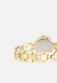 Orologio in metallo dorato con un design a bracciale robusto, caratterizzato da maglie lisce e dettagli incisi. Il retro presenta una superficie lucida.