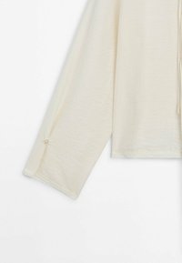 Manche longue de couleur crème avec un petit bouton près du poignet, en tissu léger et texturé.