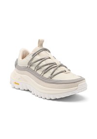 Beige- und grauer Sportschuh mit dicker weißer Profilsohle, Obermaterial aus Mesh und Wildleder sowie grauen Schnürsenkeln, die in einem Rautenmuster gebunden sind.