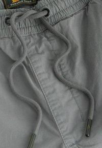 Shorts din țesătură gri, cu un braț elastic și șnur. Sforile sunt gri, cu capete metalice negre. Textură netedă și design casual.