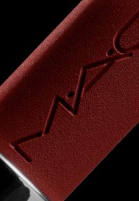 Tubo di rossetto di un rosso intenso con una finitura opaca e logo in rilievo; la parte inferiore presenta un cappuccio nero lucido.