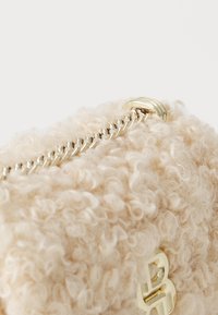 Κρεμ τσάντα με υφή, φτιαγμένη από μαλακό υλικό με κυματιστή επιφάνεια, διαθέτει χρυσαφένιο φερμουάρ και αξεσουάρ.