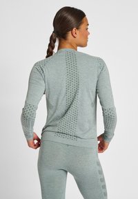 Hellgraues Sportoberteil mit strukturierten Mustern an Ärmeln und Rücken, gerippten Bündchen und taillierter Passform. Geeignet für aktive Bekleidung.