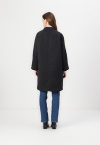 Black long coat with a collar and wide sleeves, made of smooth material. Paired with blue jeans and black platform shoes.