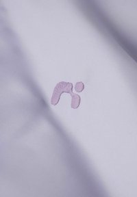 Vyšívané logo v jemně fialové barvě na hladké, jednobarevné levandulové látce; má minimalistický design s měkkou texturou.