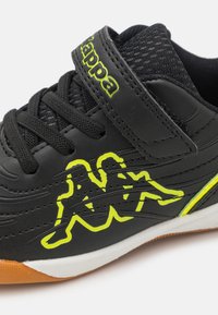 Svart Kappa-sneaker med neongul logotyp, svarta snören, mesh-tunga och en brun och vit gummisula.