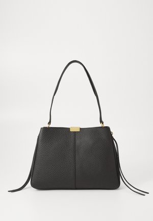 Sac à main en cuir noir texturé avec une seule poignée supérieure et une petite étiquette dorée sur fond blanc.