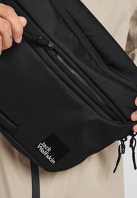 Schwarze Stoff-Schultertasche mit mehreren Reißverschlussfächern, ausgestattet mit einer glatten Textur und einem Logo-Patch mit der Aufschrift "Jack Wolfskin."