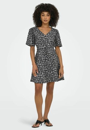 Robe à manches courtes en imprimé léopard noir et gris, avec un décolleté en V et une taille cintrée, s'évasant délicatement à l'ourlet, assortie de sandales noires.