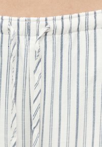 Κοντινό πλάνο λευκού υφάσματος με κάθετες λεπτές ναυτικό μπλε ρίγες και μια στριμμένη κορδόνι στο πάνω άκρο.