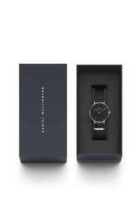 Schwarz Uhr mit rundem Ziffernblatt, silbernen Akzenten und einem schwarzen Stoffarmband, präsentiert in einer marineblauen Box mit goldener Schrift, innen mit weicher schwarzer Polsterung.